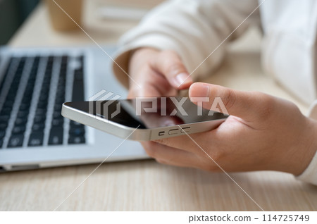 A close-up image of a woman using her smartphone at her office desk, checking messages. A close-up image of a woman using her smartphone at her office desk, checking messages. 114725749