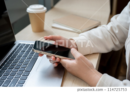 A close-up image of a woman working remotely at a coffee shop, using her smartphone. 114725753