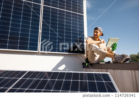 Man sitting on a rooftop with solar panels and using digital tablet Man sitting on a rooftop with solar panels and using digital tablet 114726341