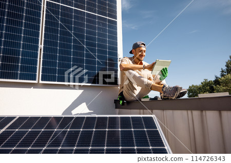 Man sitting on a rooftop with solar panels and using digital tablet Man sitting on a rooftop with solar panels and using digital tablet 114726343