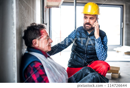 Colleague calling ambulance and giving first aid to injured worker, in pain after accident at construction site Concept of occupational safety and health in workplace. 114726644