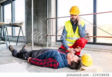 Colleague giving first aid to unconscious worker after accident, calling ambulance. Concept of occupational safety and health in workplace. Colleague giving first aid to unconscious worker after accident, calling ambulance. Concept of occupational safety and health in workplace. 114726656