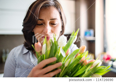 Portrait of beautiful mature woman with black hair and soft smile, holding bouquet of tulips. 114726690