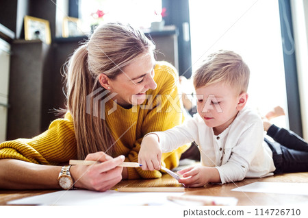 Mother drawing with son, lying on floor, holding crayons. Mom is active, creative and present in raising her son. Mother drawing with son, lying on floor, holding crayons. Mom is active, creative and present in raising her son. 114726710