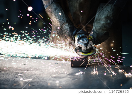 Close up of work of welder in workshop, operating welding machine, wearing protective clothing and a welding mask. Close up of work of welder in workshop, operating welding machine, wearing protective clothing and a welding mask. 114726835