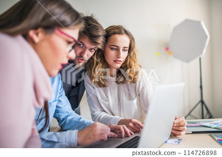 Young group of colleagues working on a new project together in a startup company office. Working in co-working space. Young group of colleagues working on a new project together in a startup company office. Working in co-working space. 114726898