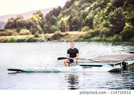 Canoeist man sitting in canoe paddling, in water. Concept of canoeing as dynamic and adventurous sport. Rear view, sportman looking at water surface, paddling 114726918