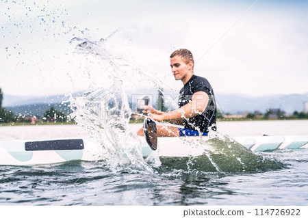Canoeist man sitting in canoe paddling, in water. Concept of canoeing as dynamic and adventurous sport. Rear view, sportman looking at water surface, paddling Canoeist man sitting in canoe paddling, in water. Concept of canoeing as dynamic and adventurous sport. Rear view, sportman looking at water surface, paddling 114726922