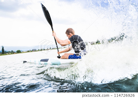 Canoeist man sitting in canoe holding paddle, in water. Concept of canoeing as dynamic and adventurous sport. Rear view, sportman looking at water surface, paddling 114726926
