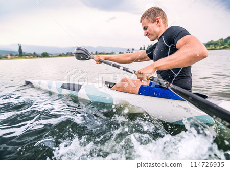 Canoeist man sitting in canoe paddling, in water. Concept of canoeing as dynamic and adventurous sport. Rear view, sportman looking at water surface, paddling Canoeist man sitting in canoe paddling, in water. Concept of canoeing as dynamic and adventurous sport. Rear view, sportman looking at water surface, paddling 114726935
