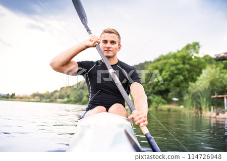 Canoeist man sitting in canoe holding paddle, in water. Concept of canoeing as dynamic and adventurous sport. Rear view, sportman looking at water surface, paddling 114726948
