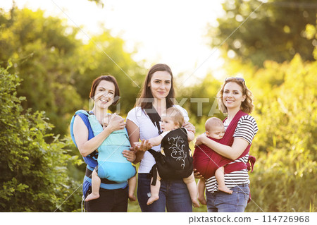 Mothers carrying babies in carriers, slings or wraps. Babywearing. 114726968