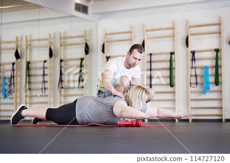Overweight woman exercising on gym mat in gym. Personal trainer couching her and helping her. Overweight woman exercising on gym mat in gym. Personal trainer couching her and helping her. 114727120