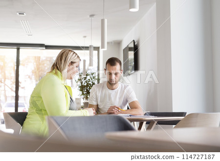 Overweight woman consulting with trainer, discussing fitness goals. Customizing exercise program with gym coach. 114727187