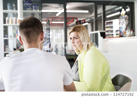 Overweight woman consulting with trainer, discussing fitness goals. Customizing exercise program with gym coach. 114727192