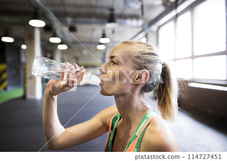 Beautiful sport woman drinking water afeter training in gym. Routine workout for woman's physical and mental health. 114727451