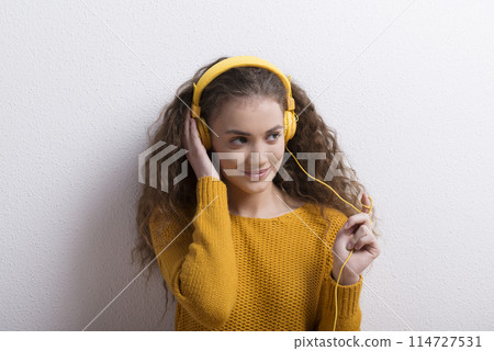Portrait of a gorgeous teenage girl with curly hair, listening music via headphones. Studio shot, white background with copy space 114727531