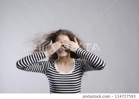Portrait of a gorgeous teenage girl with curly hair,holding hand in front of eyes. Studio shot, white background with copy space 114727593