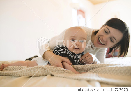 Mother playing with small baby lying on bed. Unconditional paternal love, mother's Day concept. 114727673