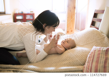 Mother playing with small baby lying on bed. Unconditional paternal love, mother's Day concept. 114727689