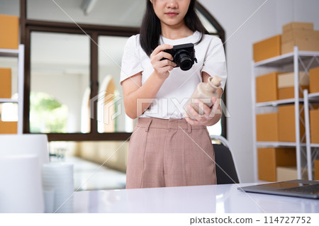 Young Asian business entrepreneur using a compact digital camera take a photo of product for upload to website online shop. Young Asian business entrepreneur using a compact digital camera take a photo of product for upload to website online shop. 114727752