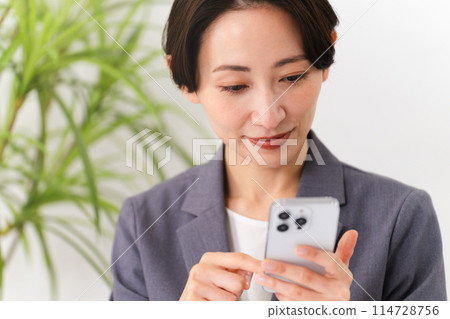 A young woman wearing a business suit operating a smartphone Business image A young woman wearing a business suit operating a smartphone Business image 114728756