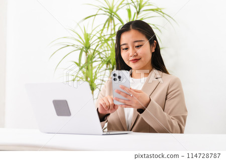 A young woman wearing a business suit and operating a laptop Business image 114728787
