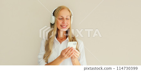 Happy smiling woman listening to music with phone in headphones on studio background 114730399