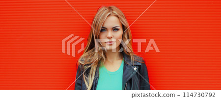 Portrait beautiful young blonde woman posing in black leather jacket on colorful orange background Portrait beautiful young blonde woman posing in black leather jacket on colorful orange background 114730792