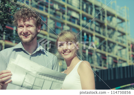 Couple on front of new house with blueprint project Couple on front of new house with blueprint project 114730856