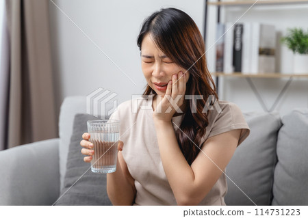 The woman with a toothache is holding her cheek in pain and a glass of water. The woman with a toothache is holding her cheek in pain and a glass of water. 114731223