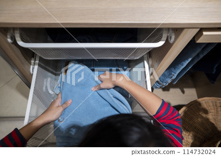Indonesian pretty teenage girls choosing clothes in wardrobe shelf at home. Asian female deciding what shirt to wear in the morning. 114732024