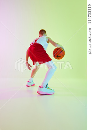Dribbling. Back view image of boy in uniform, playing basketball game, training against gradient background in neon light 114733519