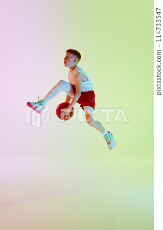 Side view full-length image of boy, basketball player during game in motion, practicing, throwing ball against gradient background in neon light Side view full-length image of boy, basketball player during game in motion, practicing, throwing ball against gradient background in neon light 114733547