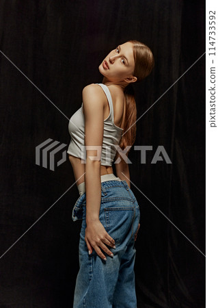 Portrait of beautiful young woman, girl wearing white casual top and jeans, posing against black background. Casual fashion line 114733592