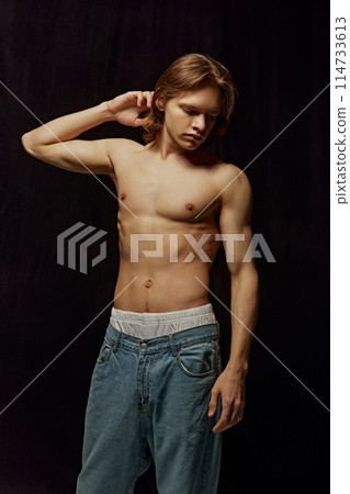 Portrait of handsome young guy posing shirtless i jeans against black background. Model with athletic, shirtless body Portrait of handsome young guy posing shirtless i jeans against black background. Model with athletic, shirtless body 114733613