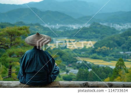 Asian peasant sits on a hill and looks into the valley Asian peasant sits on a hill and looks into the valley 114733634