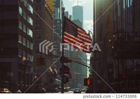 US flag flying in city street amidst towering buildings 114733806