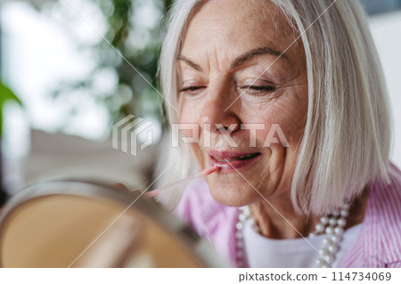 Skincare for mature woman. Portrait of beautiful older woman with gray hair putting makeup on. 114734069