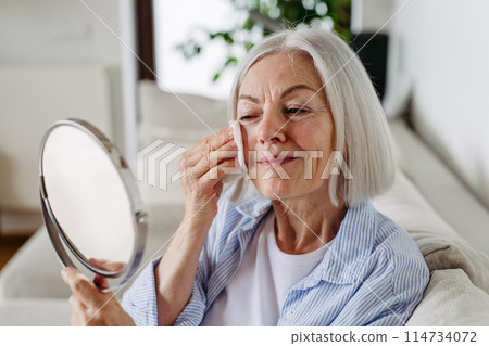 Skincare for mature woman. Portrait of beautiful older woman with gray hair cleaning, taking care of her skin. Skincare for mature woman. Portrait of beautiful older woman with gray hair cleaning, taking care of her skin. 114734072