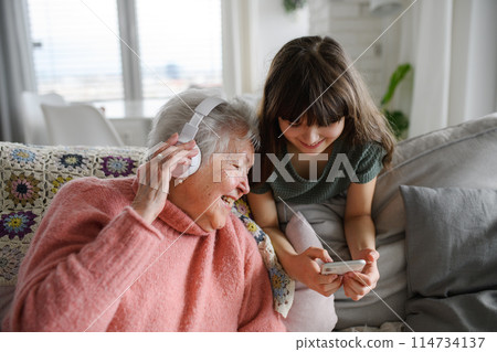 Cute girl showing funny video to gradmother. Portrait of an elderly woman spending time with granddaughter. Cute girl showing funny video to gradmother. Portrait of an elderly woman spending time with granddaughter. 114734137