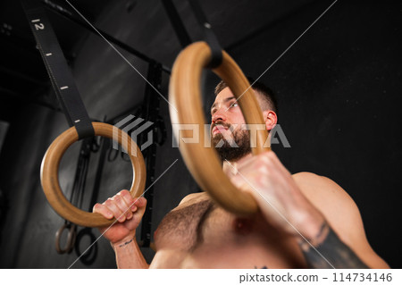 Strong man standing by rings in gym, preparing for exercising. Routine daily workout for strenght and health. 114734146