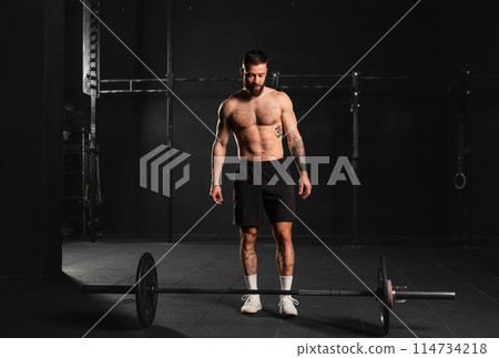 Strong man preparing for barbell lift, overhead squat, standing by barbell. Routine workout for physical and mental health. 114734218