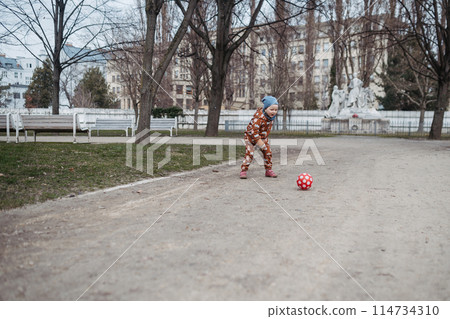 Cute toddler girl playing outdoor in playground with ball. Girl in softshell bodysuit spending time in park. 114734310