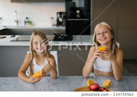 Two children sisters having breakfast and eating fresh oranges at the table in the kitchen 114734562