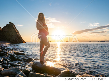 Pregnant woman enjoying sunset by the rocky beach during golden hour Pregnant woman enjoying sunset by the rocky beach during golden hour 114735093