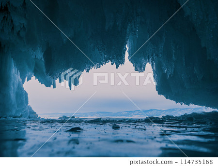 Inside a stunning ice cave on Lake Baikal, large icicles hang from the ceiling, creating a breathtaking winter landscape. Snow-covered mountains can be seen far in the distance. Inside a stunning ice cave on Lake Baikal, large icicles hang from the ceiling, creating a breathtaking winter landscape. Snow-covered mountains can be seen far in the distance. 114735168