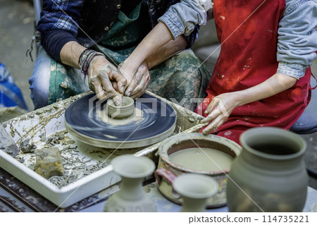 Man and a child are making pottery. The man is teaching the child how to make pot 114735221
