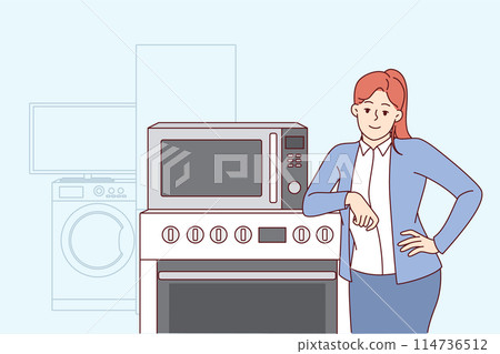 Woman selling household appliances stands near oven and washing machine and looks at camera 114736512