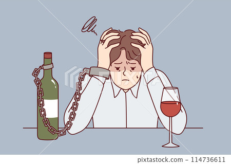 Man suffering from alcohol addiction is chained to bottle of wine, sitting at table clutching head Man suffering from alcohol addiction is chained to bottle of wine, sitting at table clutching head 114736611